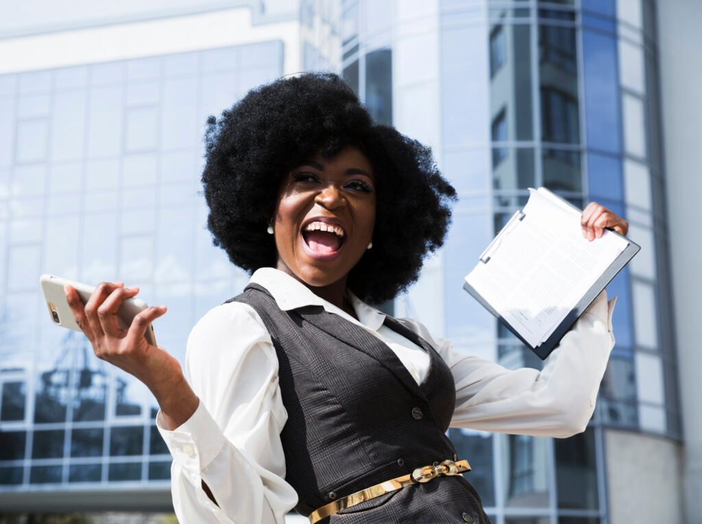 excited young african businesswoman holding mobile phone clipboard