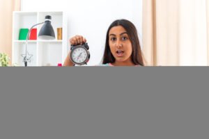 young girl casual clothes holding alarm clock clenching fist happy excited sitting chair light living room 1